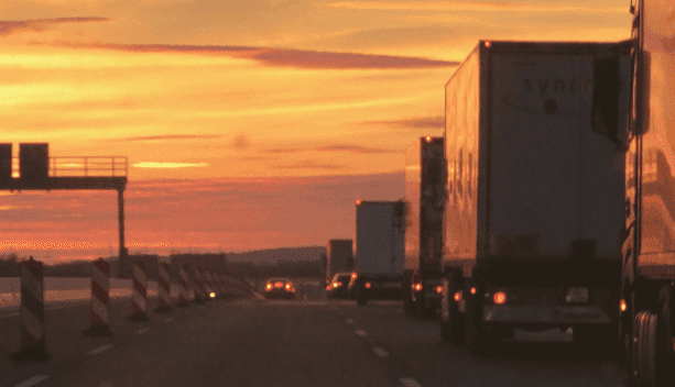 Highway filled with semi-trucks and cars at sunset, featuring an orange and yellow sky.