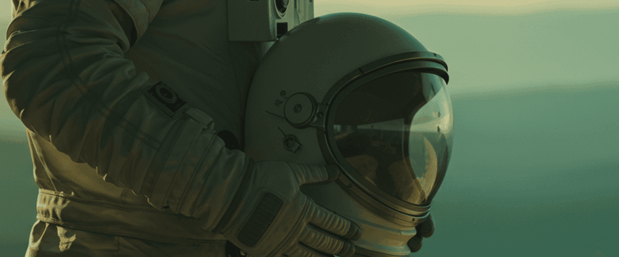 An astronaut in a spacesuit holds a helmet with a reflective visor against a warm, blurry landscape.