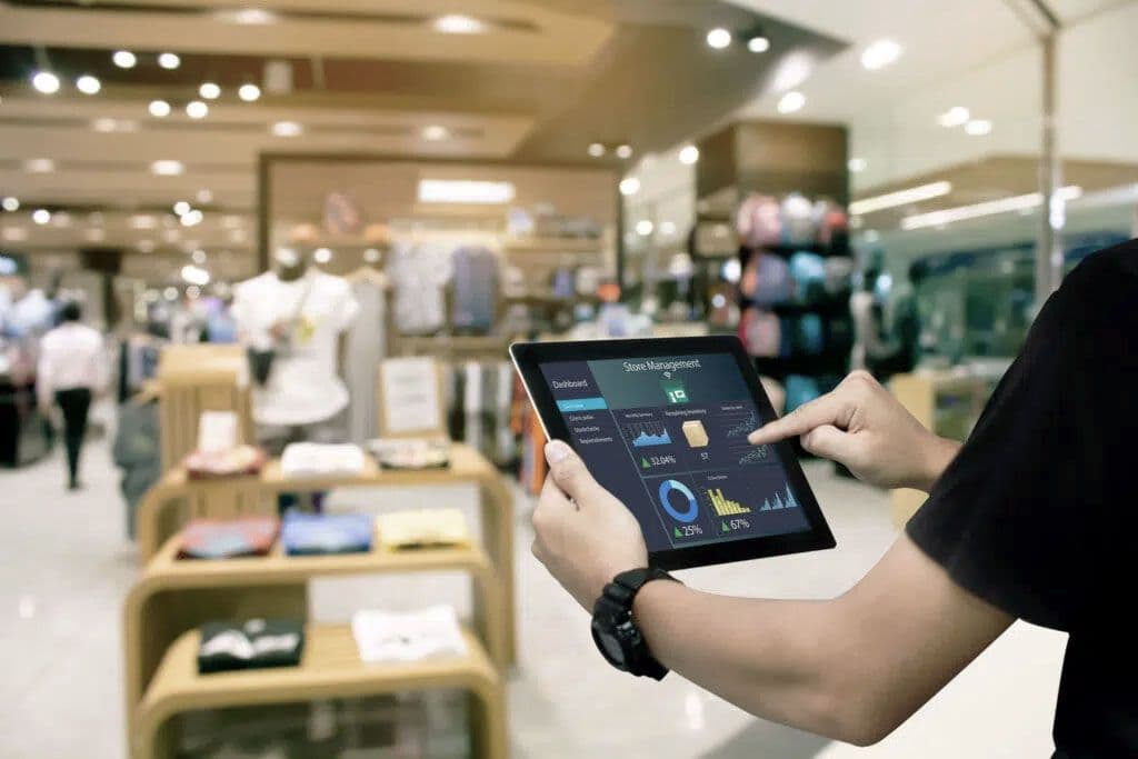 A clothing store with the arm of an employee pointing out something on a tablet.