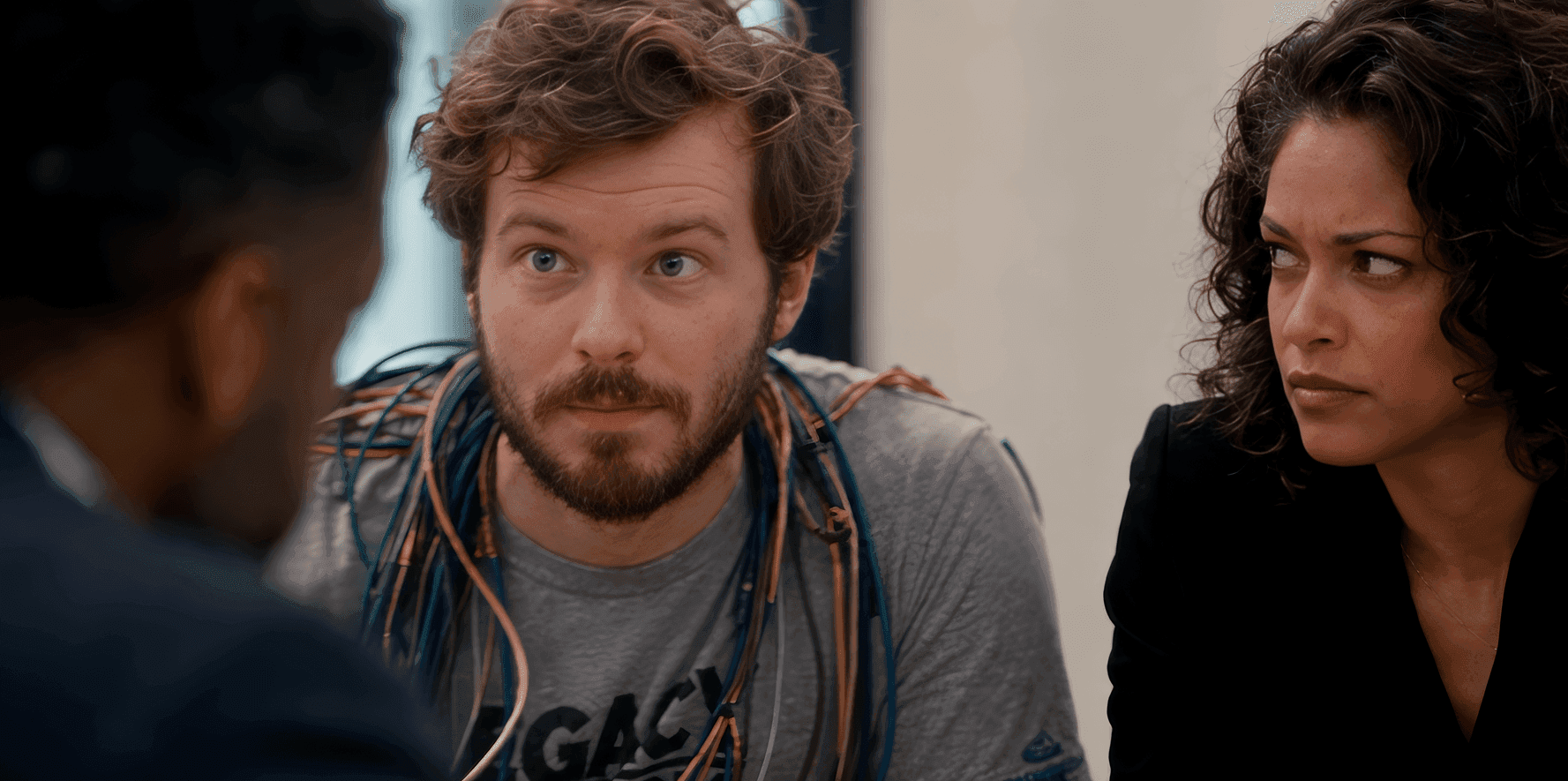 A man with curly hair and wires around his neck listens intently during a meeting.