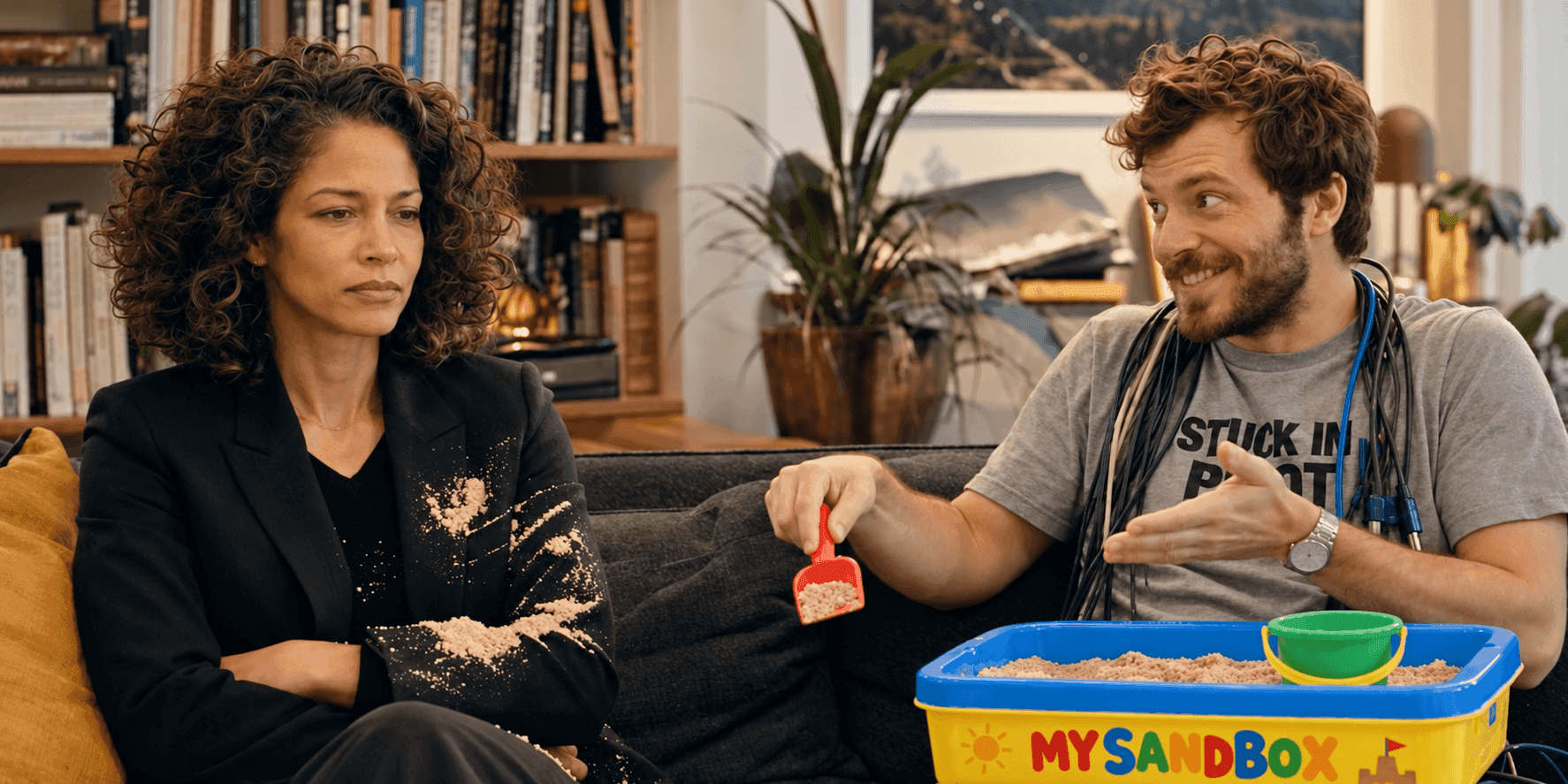 A displeased woman with sand on her jacket sits next to a man with a sandbox.